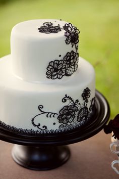 two tiered cake with black and white designs on it sitting on a table outside