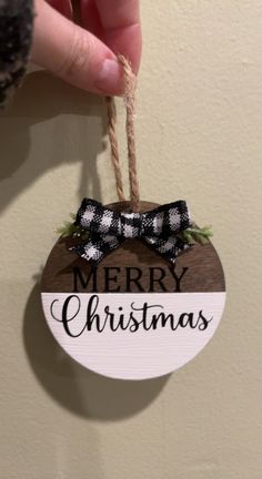 a hand holding a merry christmas ornament hanging from a string on a wall