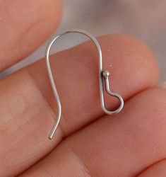 a person is holding an open silver earring in their hand, with the end of it