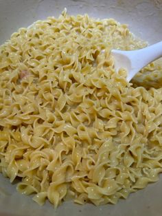 a bowl filled with pasta and sauce on top of a table next to a white spoon