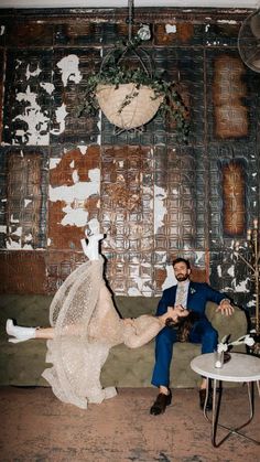 a man and woman sitting on a couch in front of a wall with peeling paint