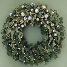 a green wreath with silver ornaments and greenery on the front is hung on a wall