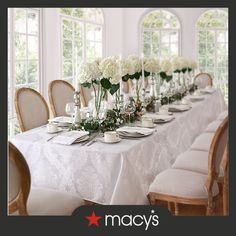 a long table with white flowers in vases and plates on it is surrounded by chairs