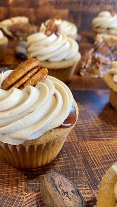 cupcakes with white frosting and pecans on the side sitting on a wooden table