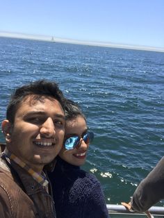 two people taking a selfie on a boat in the ocean with blue sky and water behind them