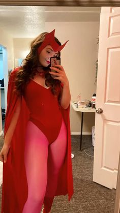 a woman in a red cape and pink bodysuit taking a selfie with her cell phone