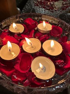 several candles are lit in a bowl filled with water and rose petals on a table