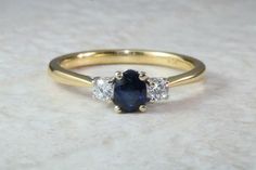 a three stone ring with an oval blue sapphire surrounded by smaller round diamonds on a white marble surface