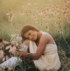 a woman is sitting in the grass with her arms around her chest and holding flowers