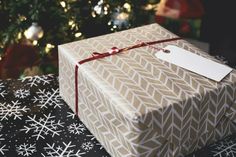 a gift wrapped in brown and white paper with a red ribbon is sitting next to a christmas tree