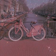 a pink bicycle parked on the side of a brick road next to water and buildings