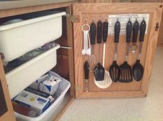 an open cabinet with utensils and other kitchen items in it on the floor