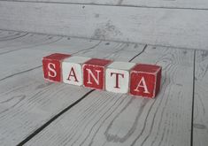 wooden blocks spelling the word santa on a white wood floor with red and white letters