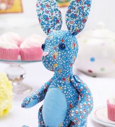 a blue stuffed animal sitting on top of a table next to cupcakes and cake