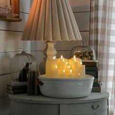 several lit candles sit in a bowl on a table next to a lamp and books