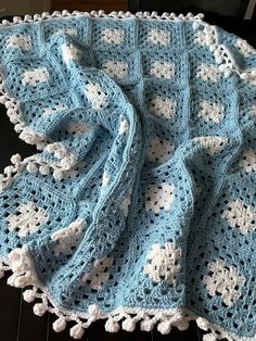 a blue and white crocheted blanket sitting on top of a wooden floor next to a black table