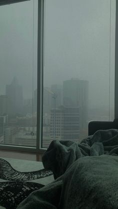 a bed in front of a window with a blanket on top of it and the city outside