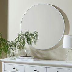 a round mirror sitting on top of a white dresser next to a potted plant