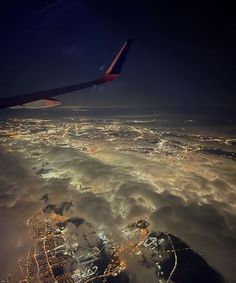 an airplane wing flying over the city lights at night in the sky above the clouds