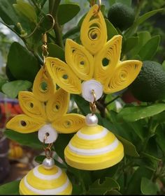 two yellow and white earrings hanging from a tree with green leaves in the back ground