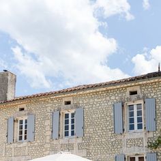 an old stone building with blue shutters and white umbrella in front of it on a sunny day