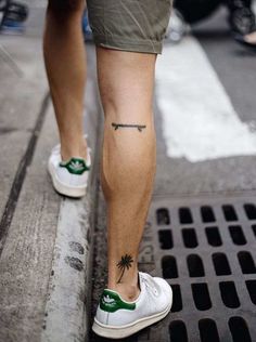 a person with a cross tattoo on their left leg and green shoes is walking down the street