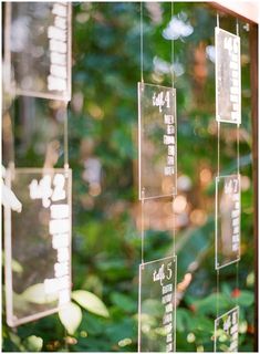 there are many signs hanging on the glass wall in front of some trees and bushes