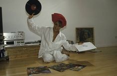 a woman sitting on the floor holding up a record in front of her face and wearing a red hat