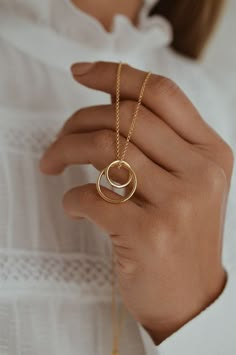 a close up of a person's hand holding a necklace with two rings on it