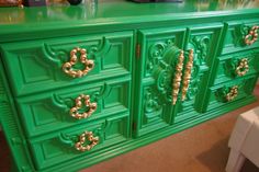 a green dresser with gold handles and drawers