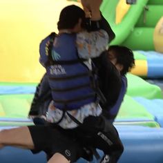 two people in life vests hug while jumping on an inflatable obstacle course