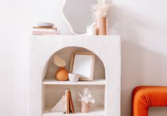 an orange chair sitting next to a white shelf with books and vases on it