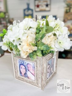 a vase filled with white flowers on top of a table next to a framed photo