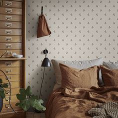 a bed sitting next to a wooden dresser in a room with wall paper on the walls