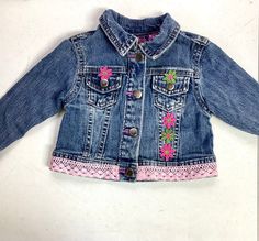 a blue jean jacket with pink flowers on the front and back, sitting on a white surface