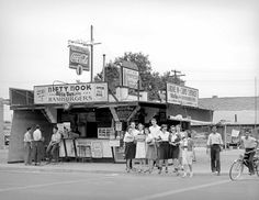 black and white photograph of people standing in front of a food stand