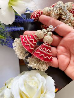 a person is holding two red and gold brooches in their hand next to some flowers