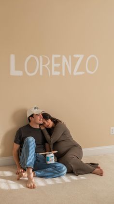 a man and woman sitting on the floor in front of a wall with words written on it