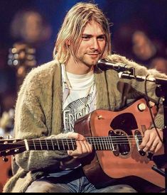 a man sitting in front of a microphone while holding a guitar