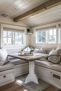 a table with some pillows on top of it in front of two windows and a bench