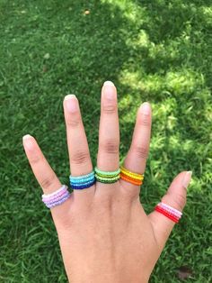 a person's hand with four different colored bracelets on it, in the grass