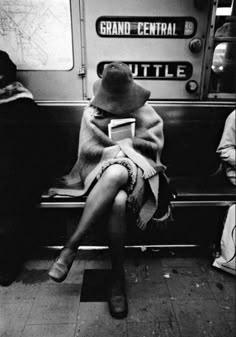 a person sitting on a subway with a hat and blanket wrapped around their head, reading a book