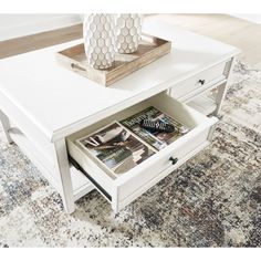 a white coffee table with magazines in the drawer and a vase sitting on top of it