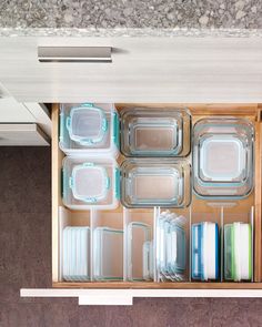 an open drawer filled with glass dishes and containers on top of a counter next to a wall