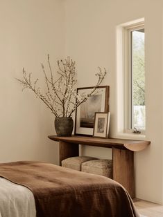 a bedroom with a bed, table and pictures on the wall next to it in front of a window