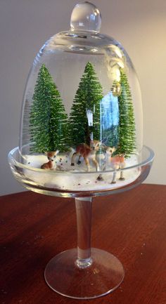 a glass dome with trees and animals in it on a wooden table next to a white wall