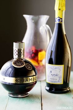 two bottles of alcohol sit on a table next to a vase with fruit in it