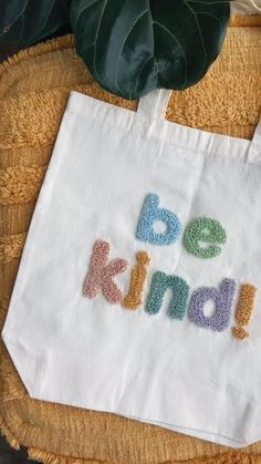 a white bag with the words be kind on it sitting next to a plant and some leaves