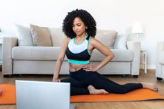 a woman sitting on an orange yoga mat in front of a laptop