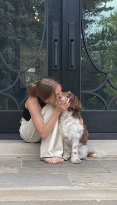 a woman is kissing her dog on the front steps with an iron door in the background